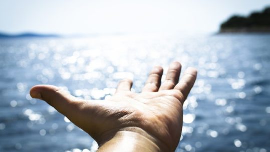 Hand reaching out over water symbolising the receiving of counselling support during depression